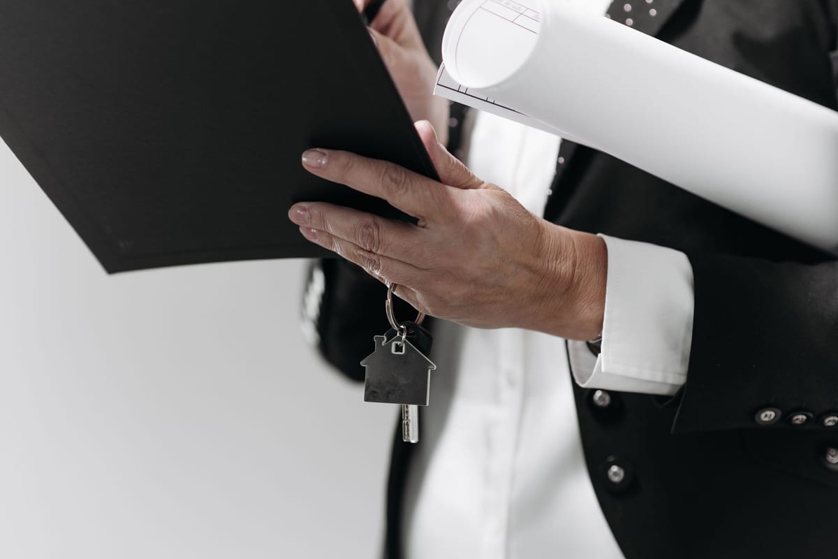 A hand holding a house key over architectural plans, representing the transfer of a property's khata record into the new owner's name